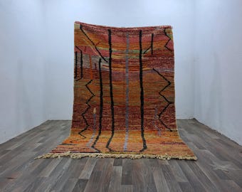 May include: A rectangular area rug featuring a vibrant gradient of orange, red, and yellow horizontal stripes. The design includes bold, black vertical lines and jagged, zigzagging black patterns throughout the surface, finished with a fringe edge.