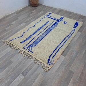 May include: A white and blue Moroccan rug with a geometric design. The rug has a fringe border and is made of wool.