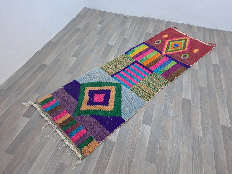 May include: A colorful, geometric patterned rug with a variety of colors including red, orange, yellow, green, blue, purple, and brown. The rug has a fringe on the edges.