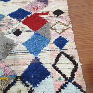 May include: A colorful Moroccan rug with a geometric pattern in shades of blue, red, pink, and brown. The rug has a fringe border and is made of wool.