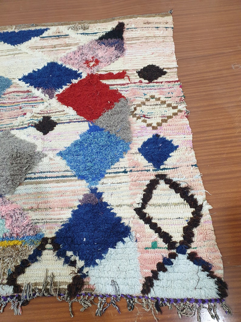 May include: A colorful Moroccan rug with a geometric pattern in shades of blue, red, pink, and brown. The rug has a fringe border and is made of wool.