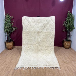 Peut inclure: Un tapis marocain blanc avec un motif en losanges. Le tapis a une bordure en franges et est fait de laine.