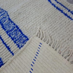 May include: A white and blue woven rug with fringe. The rug has a geometric pattern of blue stripes on a white background.