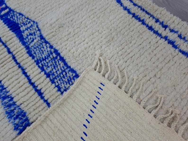 May include: A white and blue woven rug with fringe. The rug has a geometric pattern of blue stripes on a white background.