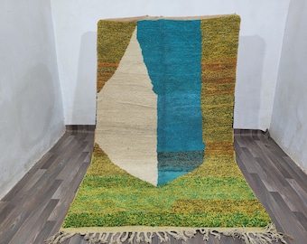 Könnte beinhalten: Ein farbenfroher marokkanischer Teppich mit geometrischem Muster in Grün-, Blau-, Weiß- und Orangetönen. Der Teppich hat einen Fransenrand.