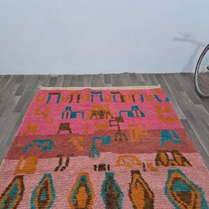 May include: A pink, orange, blue, and brown patterned rug with geometric designs. The rug has a fringe border.
