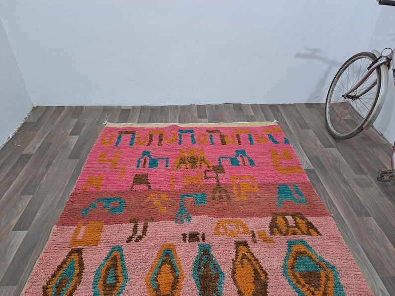 May include: A pink, orange, blue, and brown patterned rug with geometric designs. The rug has a fringe border.