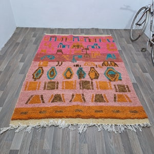 May include: A colorful Moroccan rug with a geometric pattern in shades of pink, orange, brown, and blue. The rug has a fringe border and is made of wool.