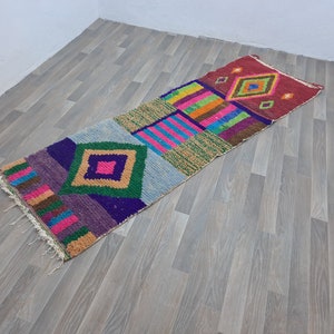 May include: A colorful, geometric patterned rug with a long, rectangular shape. The rug features a variety of colors, including red, pink, blue, green, and yellow. The rug is made of a soft, woven material and has a fringed edge.