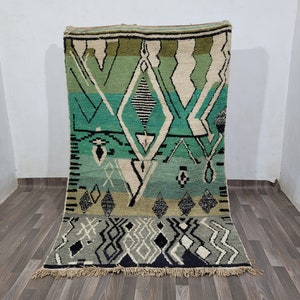 May include: A green, white, and black Moroccan rug with a geometric pattern. The rug has a fringe border.