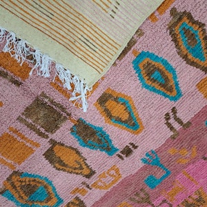May include: Two woven rugs with a pink, orange, brown, and blue geometric pattern. The rugs have fringe on the edges.