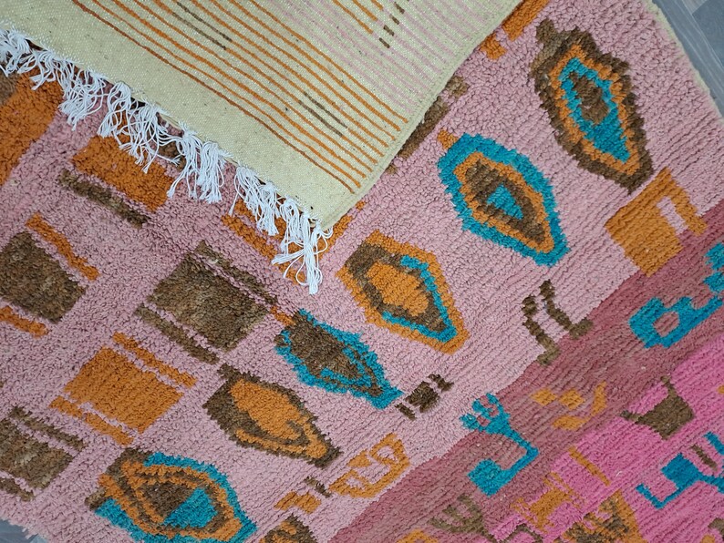 May include: Two woven rugs with a pink, orange, brown, and blue geometric pattern. The rugs have fringe on the edges.