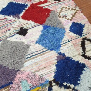 May include: A colorful, handwoven rug with a patchwork design. The rug features various shades of blue, red, pink, gray, and brown. The rug is made of wool and has a fringed edge.