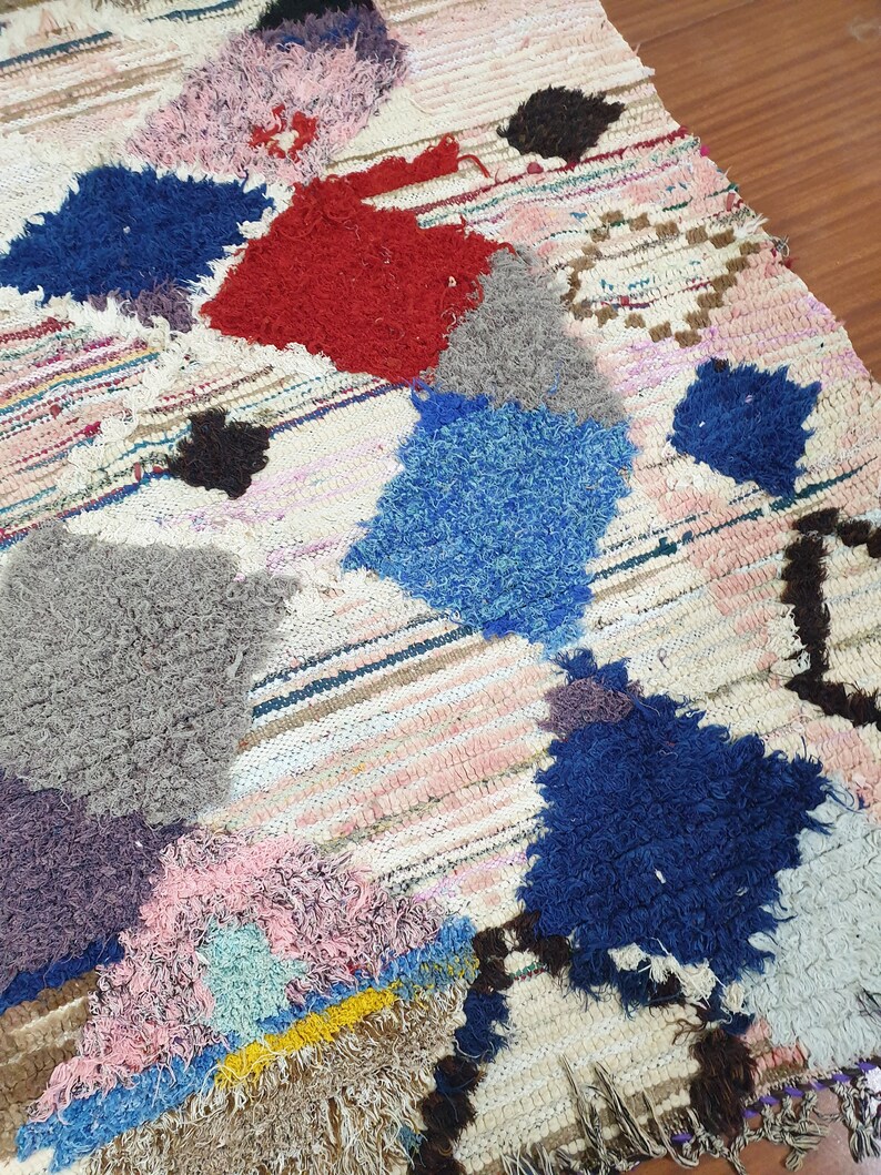 May include: A colorful, handwoven rug with a patchwork design. The rug features various shades of blue, red, pink, gray, and brown. The rug is made of wool and has a fringed edge.
