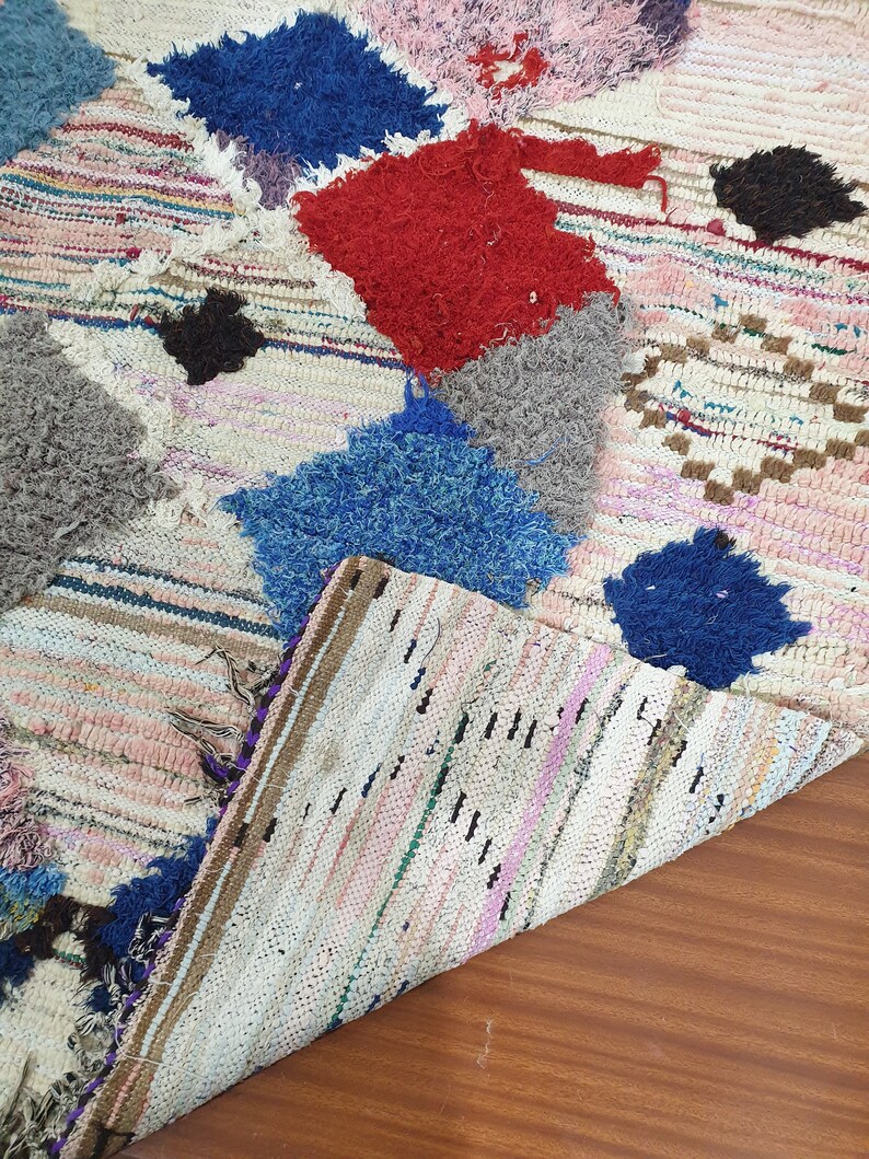 May include: A white, handwoven rug with colorful patches of blue, red, gray, and black. The rug has a striped pattern and is made of recycled materials.