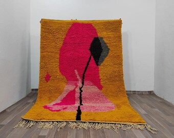 May include: A rectangular area rug featuring a deep mustard yellow background with a large, central abstract design in vibrant hot pink, light pink, and black. The rug has a thick, shaggy pile texture and includes decorative fringe along the bottom edge.