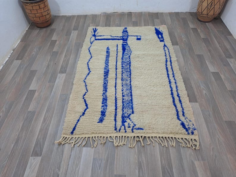 May include: A white and blue Moroccan rug with a geometric design. The rug has a fringe border and is made of wool.