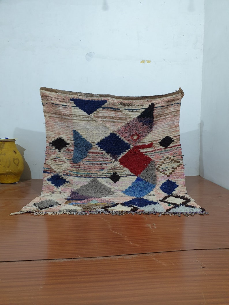 May include: A colorful Moroccan rug with a geometric pattern in shades of blue, red, pink, and white. The rug has a fringe border and is made of wool.