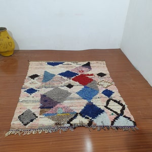 May include: A colorful Moroccan rug with geometric patterns in shades of blue, red, pink, and gray. The rug has a white background and a fringe border.