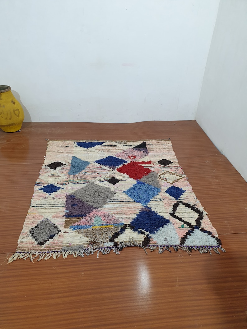 May include: A colorful Moroccan rug with geometric patterns in shades of blue, red, pink, and gray. The rug has a white background and a fringe border.