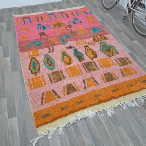 May include: A pink, orange, and blue patterned rug with a fringe border. The rug has a geometric design with abstract shapes.