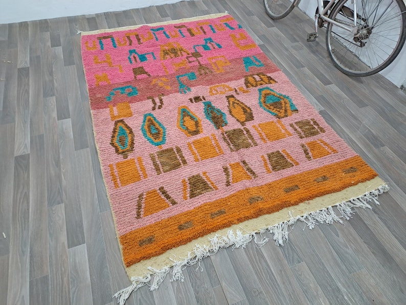 May include: A pink, orange, and blue patterned rug with a fringe border. The rug has a geometric design with abstract shapes.