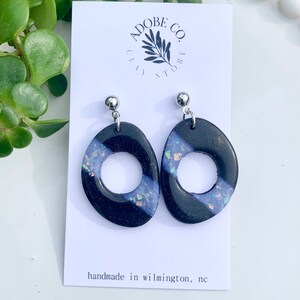 Könnte beinhalten: Schwarze und weiße ovale Ohrringe mit schimmernden Glitzerakzenten. Die Ohrringe haben einen silbernen Stift und eine silberne Rückseite. Die Ohrringe sind handgefertigt in Wilmington, North Carolina.