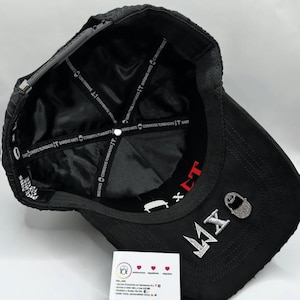 Puede incluir: Gorra de b&eacute;isbol negra con el texto "MX" en pedrer&iacute;a plateada. La gorra tiene una visera curva y un forro de sat&eacute;n negro con texto blanco. Tambi&eacute;n tiene el texto "BARBAS HATS CORRIDOS TUMBADOS IT BARE".