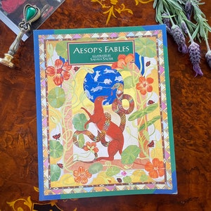 May include: A book titled "Aesop's Fables" illustrated by Saraya Salter. The cover features a colorful illustration of a fox and a snake in a garden setting.