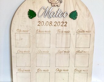 Puede incluir: Un gráfico de crecimiento de madera con un diseño de león y hojas. El gráfico tiene 12 cuadrados para marcar el crecimiento de un niño cada mes. El gráfico está personalizado con el nombre "Mateo" y la fecha "20.08.2022".