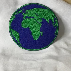 May include: A blue and green embroidered patch of the Earth. The continents are green and the oceans are blue.