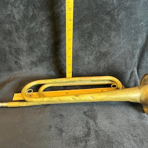 May include: A vintage brass bugle with a silver mouthpiece and a flared bell. A yellow ruler is placed next to the bugle. The bugle is approximately 10 inches long.