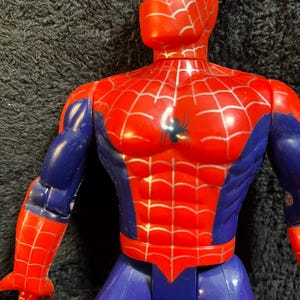 May include: A red, blue, and silver Spider-Man action figure. The figure has a red head and torso with a silver web design. The arms are red and blue, and the legs are blue. A black spider emblem is on the chest.