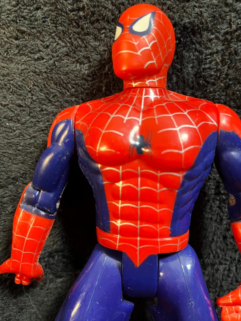 May include: A red, blue, and silver Spider-Man action figure. The figure has a red head and torso with a silver web design. The arms are red and blue, and the legs are blue. A black spider emblem is on the chest.