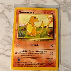 May include: A Charmander Pokémon trading card. The card features an orange lizard-like creature with a flame on its tail. The card has the text "Charmander" and "50 HP". The card is 2 feet long and weighs 19 lbs.