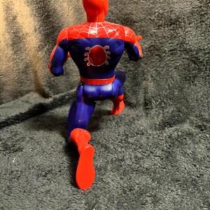 May include: A plastic action figure of Spider-Man in a running pose. The figure is primarily red and blue, with a spider emblem on the back. The figure is approximately 6 inches tall.