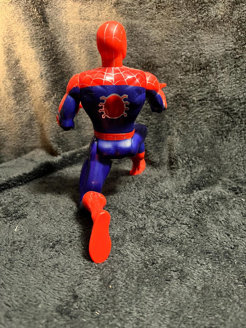May include: A plastic action figure of Spider-Man in a running pose. The figure is primarily red and blue, with a spider emblem on the back. The figure is approximately 6 inches tall.