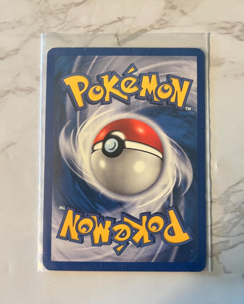 以下が含まれることがあります： 保護スリーブに入ったポケモンカード。カードの青い背景には、黄色のポケモンロゴと赤と白のモンスターボールのデザインがあります。カードは長方形です。