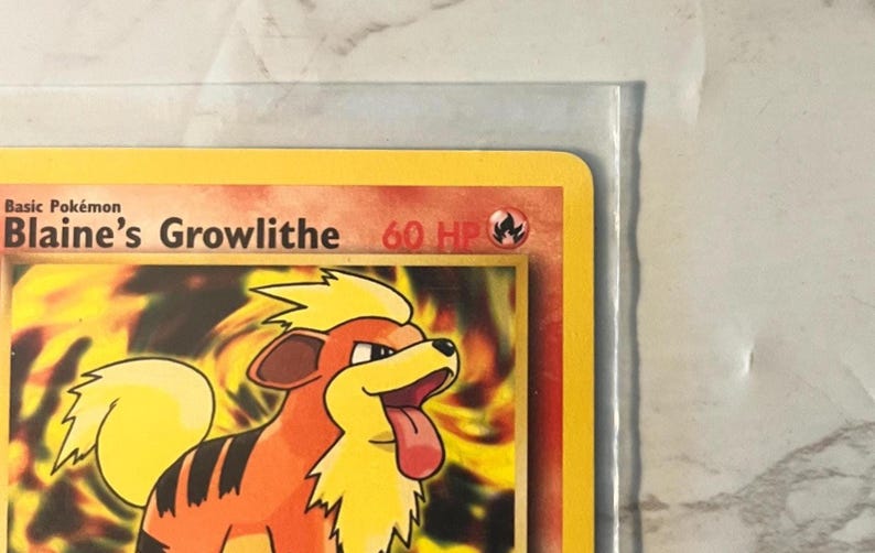 以下が含まれることがあります： ブレイズのガーディが描かれたポケモンカード。カードは黄色の縁取りで、オレンジ、茶色、黄色の色でガーディのイラストが表示されています。「Basic Pok&eacute;mon」と「60 HP」の文字が見えます。