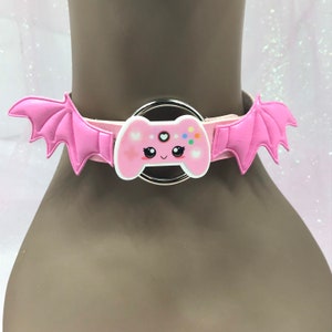 May include: Pink choker necklace with a cute cartoon video game controller charm and bat wings on either side.