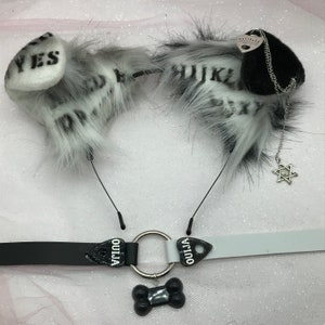May include: Black and white furry ear headband with a black and white ouija board charm and a silver star charm. The headband is attached to a black and white choker with a black bone charm.