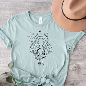 Puede incluir: Una camiseta azul claro con un dise&ntilde;o gr&aacute;fico en blanco y negro de una mujer con una mariposa y flores. El gr&aacute;fico tambi&eacute;n incluye el texto "VIRGO".