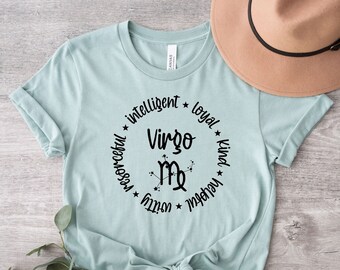 Può includere: Una maglietta blu chiaro con una grafica circolare nera che presenta il segno zodiacale della Vergine e le parole "Vergine", "intelligente", "leale", "gentile", "utile", "risorsa", "arguto".