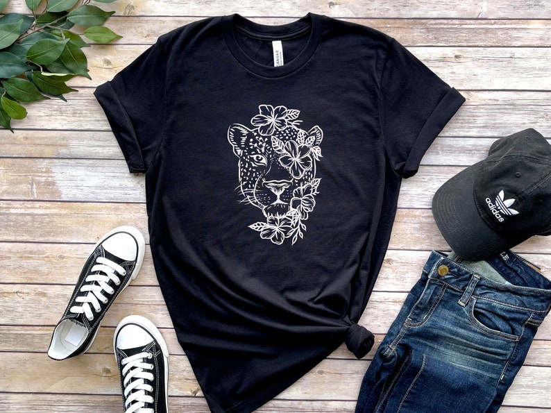 May include: Black t-shirt with a white graphic of a jaguar's face surrounded by flowers.