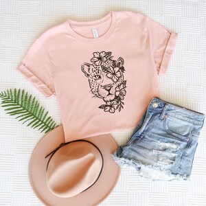 May include: A pink t-shirt with a black and white illustration of a jaguar's face with flowers around it.