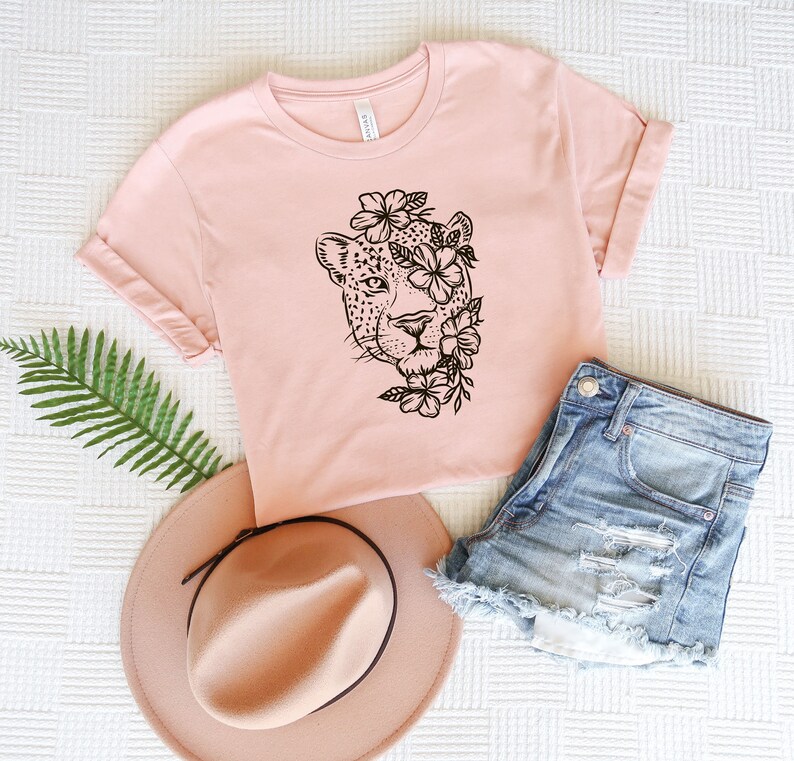 May include: A pink t-shirt with a black and white illustration of a jaguar's face with flowers around it.