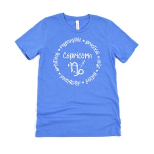 May include: A blue t-shirt with a white circle design featuring the zodiac sign Capricorn and the words "Capricorn", "ambitious", "responsible", "practical", "patient", "wise", "determined", "grounded".