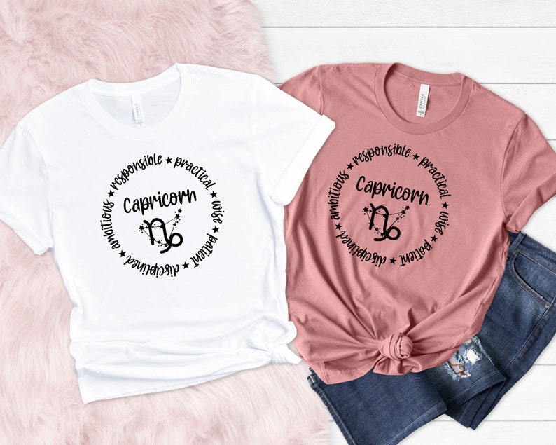 May include: Two t-shirts with a black circle design featuring the Capricorn zodiac symbol and the words "Capricorn", "ambitious", "responsible", "practical", "wise", "patient", and "disciplined".