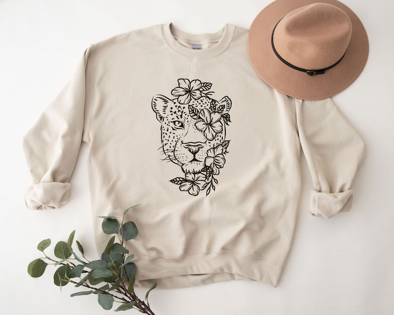 May include: A beige sweatshirt with a black and white graphic of a leopard's face surrounded by flowers.
