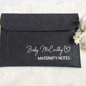 May include: A dark grey felt envelope with a white inscription that reads "Baby McCarthy" with a heart symbol and "Maternity Notes".